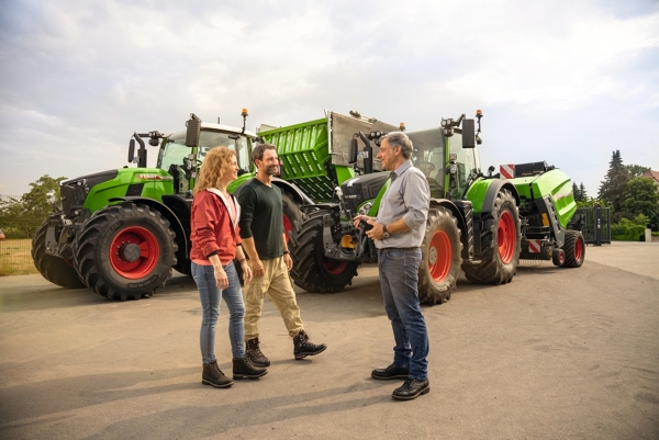 A male and female farmer standing with a dealer in front of two tractors and preparing for the test drive.