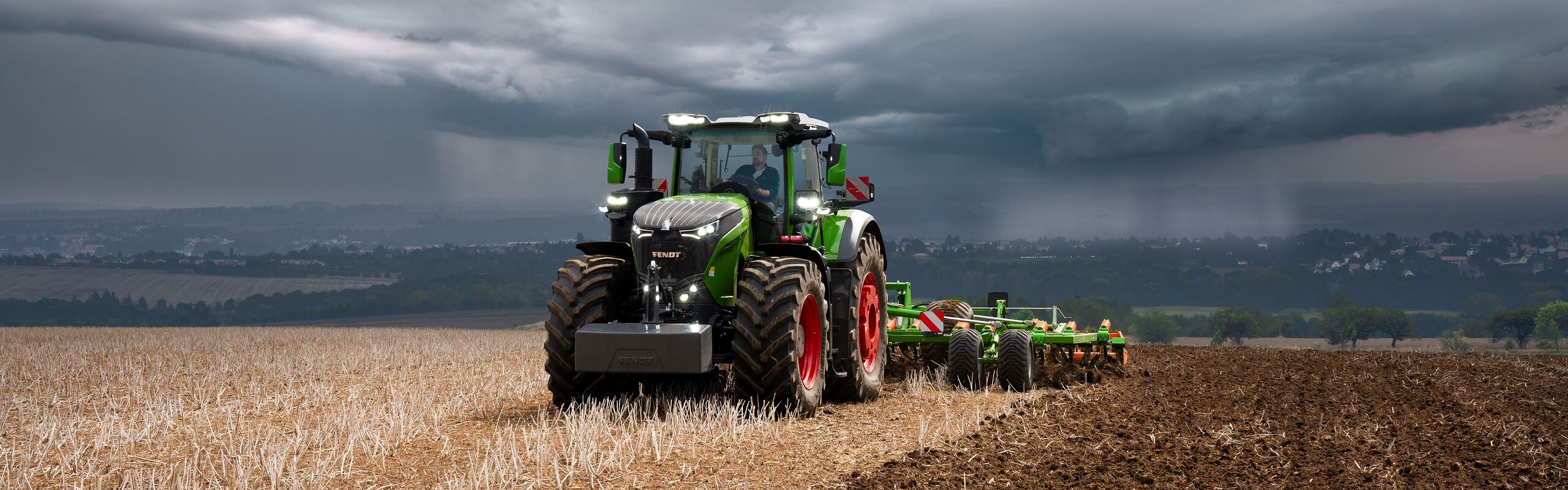 The Fendt 1000 Vario tractor is still doing field work at full power against heavy approaching storm clouds.