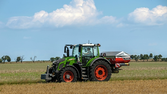 The green Fendt 600 Vario tractor with red rims seen from the side on a green meadow. A blue sky with white clouds can be seen in the background.