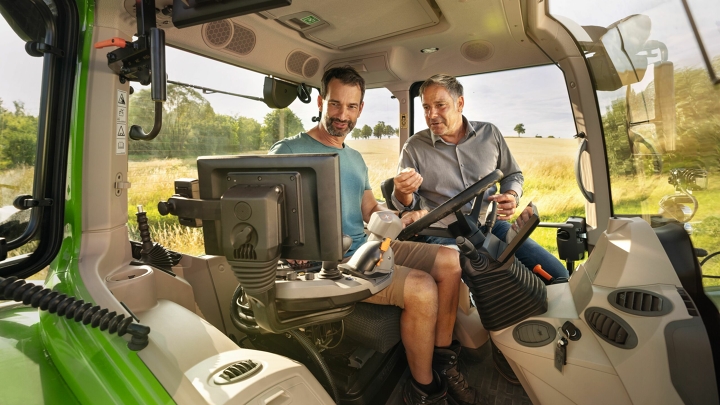 A Fendt dealer in the cab of a green Fendt tractor demonstration model at a farmer customer's property