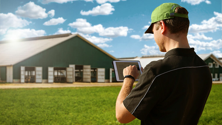 A farmer stands in front of his farm with tablet in hand and is signing up for the Fendt newsletter