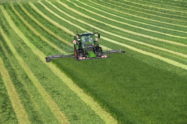 The green Fendt 600 Vario tractor mowing with the green Fendt Slicer implement on a green meadow; the mowing tracks can be seen in the background.