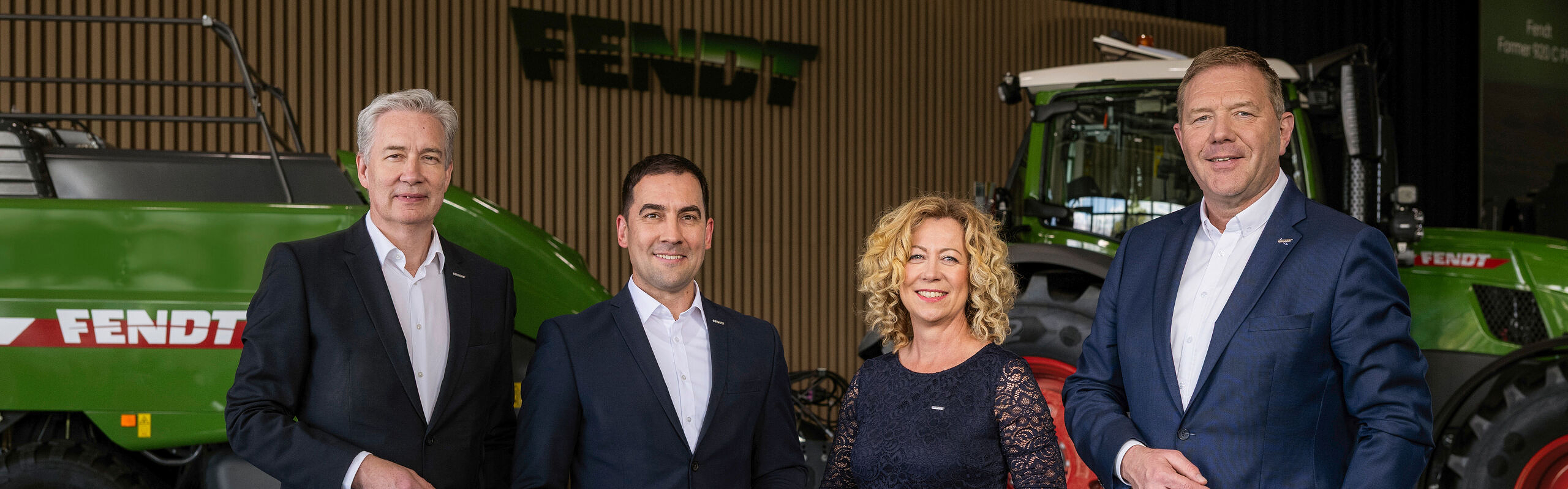 From left to right, Managing Directors Ekkehart Gläser, Dr Josef Mayer, Ingrid Bußjäger-Martin and Christoph Gröblinghoff stand next to each other in the Fendt Forum in front of a Fendt tractor and the Fendt square baler