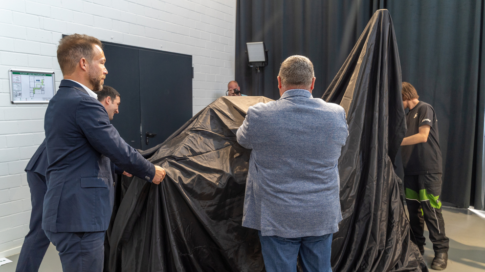Dr Josef Mayer & Alexander Schenk (Fendt) and Sven Borchert and an apprentice unveil the Fendt dispensing station Four men pull on a black cloth, revealing the Fendt dispensing station underneath