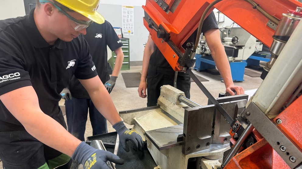 3 men (apprentices) stand at a band sawing machine and saw