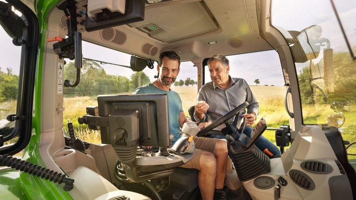 A Fendt dealer in the cab of a green Fendt tractor demonstration model at a farmer customer's premises