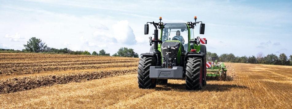 The Fendt 700 Vario Gen 7 in use in a field. In the background are trees and a blue sky with white clouds.