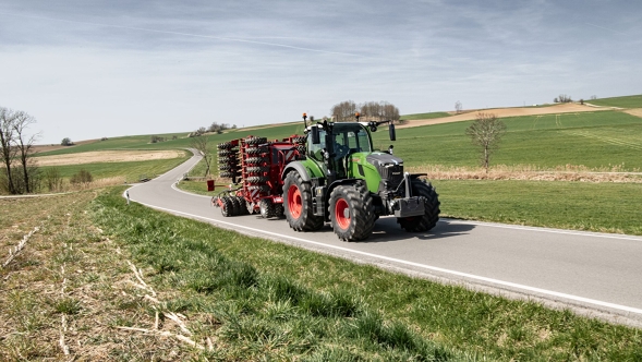 Fendt 700 Vario Gen7.1 with transport device on the road in a rural setting. Fendt 700 Vario Gen7.1 with attached implement driving on a country road through hilly spring landscape.