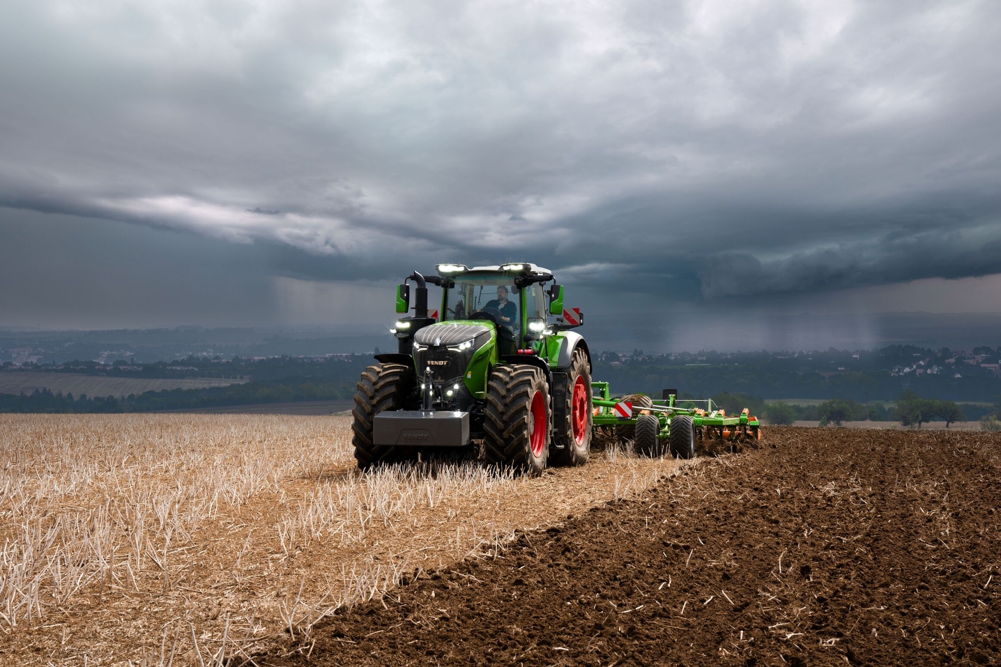 The Fendt 1000 Vario tractor is still doing field work at full power against heavy approaching storm clouds.