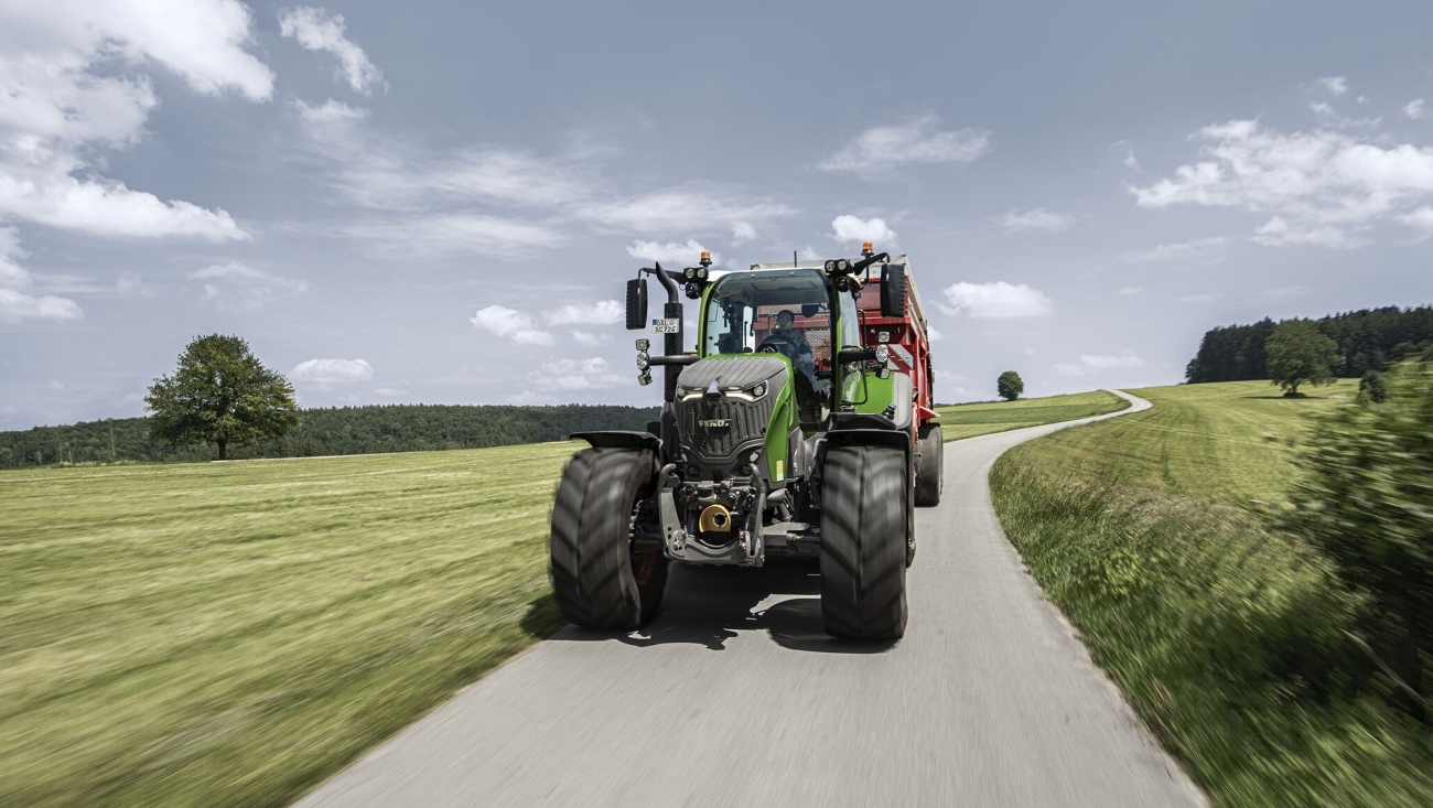 A Fendt 700 Vario Gen7.1 with attached forage wagon on a country road in the summer