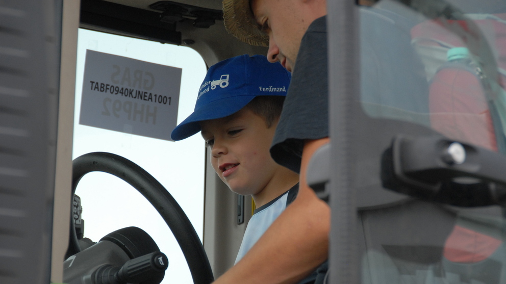 A little boy gets to sit on the driver's seat of a tractor