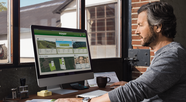 Dark-haired middle-aged man sits at a desk in front of the screen and looks at the Fendt TaskDoc