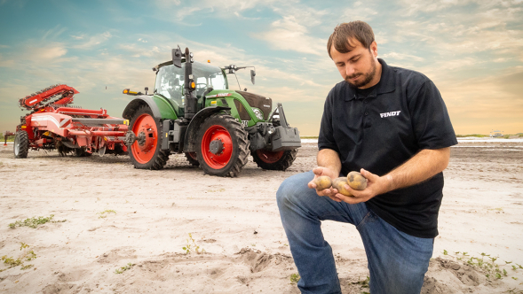 Male Farmer holds potatoes in his sandy field with a Fendt tractor in the background