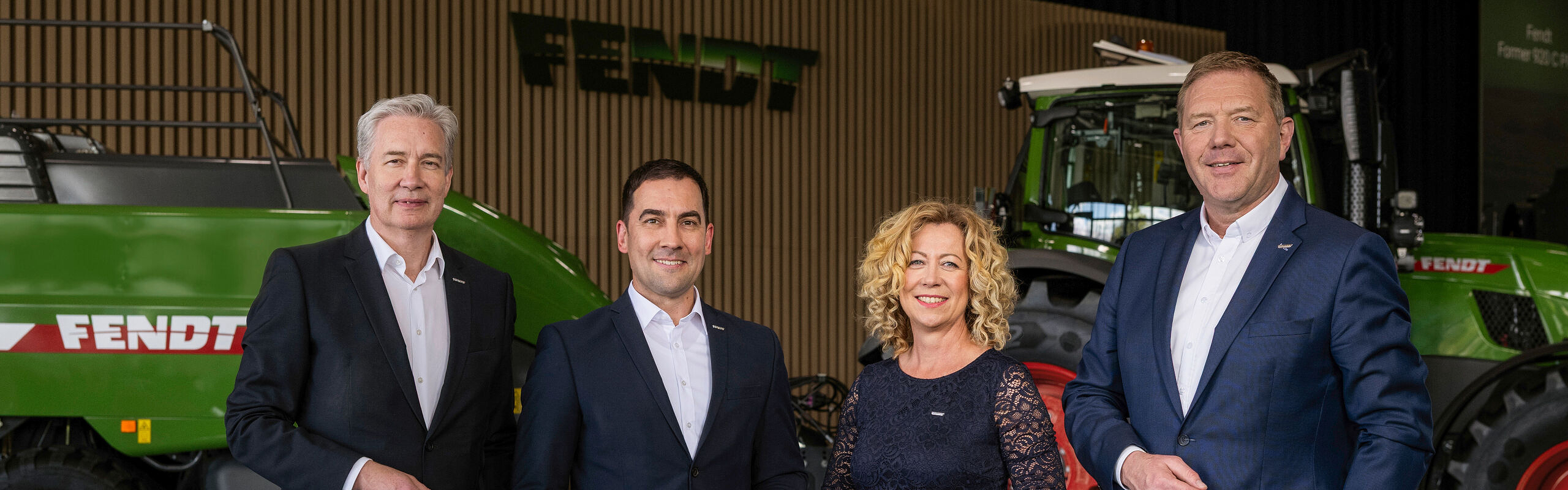 From left to right, Managing Directors Ekkehart Gläser, Dr Josef Mayer, Ingrid Bußjäger-Martin and Christoph Gröblinghoff stand next to each other in the Fendt Forum in front of a Fendt tractor and the Fendt square baler