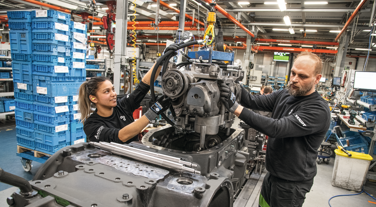 Two skilled workers assemble a tractor gearbox together in a modern workshop.