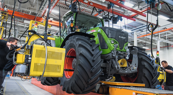 Employees assemble a Fendt tractor in a production line with the support of automated tools.