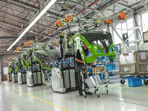 Production hall with several Fendt tractor cabs in a row on the assembly line. Employees work on the cabs while modern laser technology ensures precise contours and top quality.