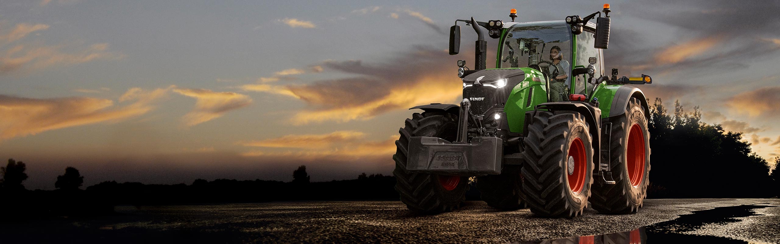 Female Farmer driving a Fendt 700 Tractor in the dusk on a wet road