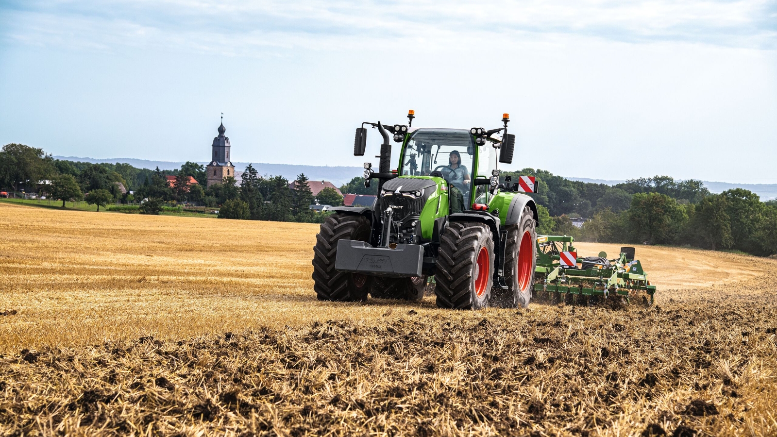 A farmer driving a Fendt 700 Vario Gen7 and a cultivator in a field.