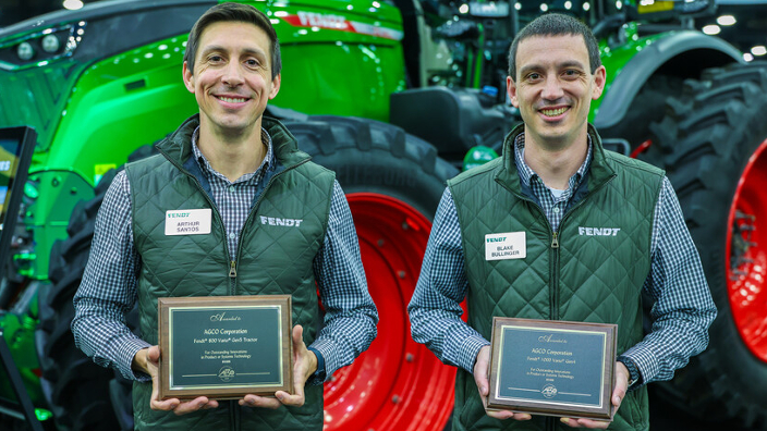 Two Fendt product specialists standing in front of the Fendt 1000 Vario holding the AE50 award plaques